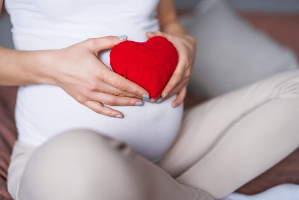 Pregnant woman holding a red heart over her abdomen.