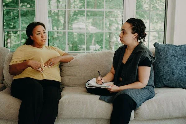 Two women sit on a couch, one is pregnant.